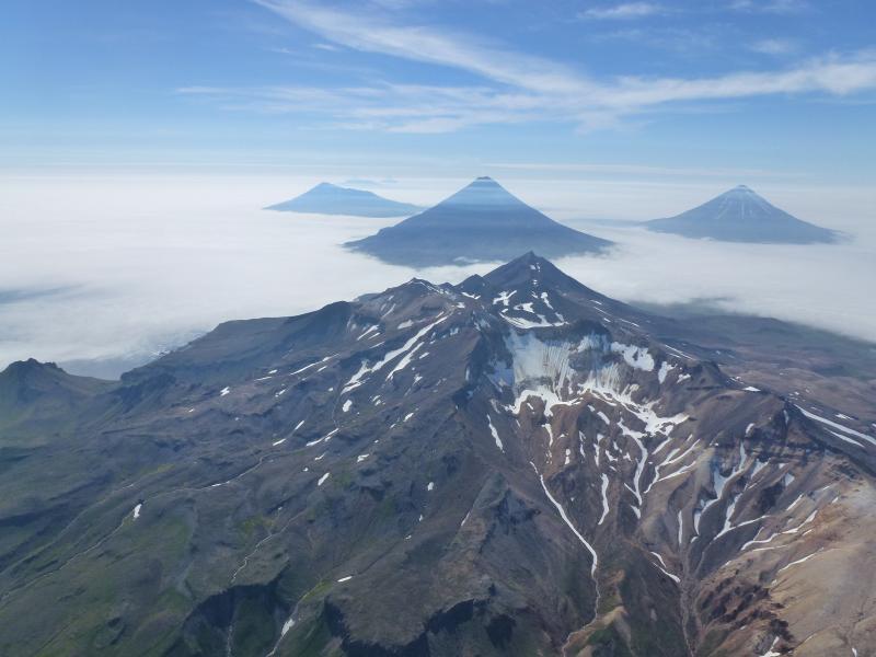 An aerial oblique photo of the volcanoes in the Islands of Four Mountains, Alaska, taken in July 2014. In the center is the summit of Mount Tana. Behind Tana are (left to right) Herbert, Cleveland, and Carlisle Volcanoes. Credit: John Lyons/USGS. 