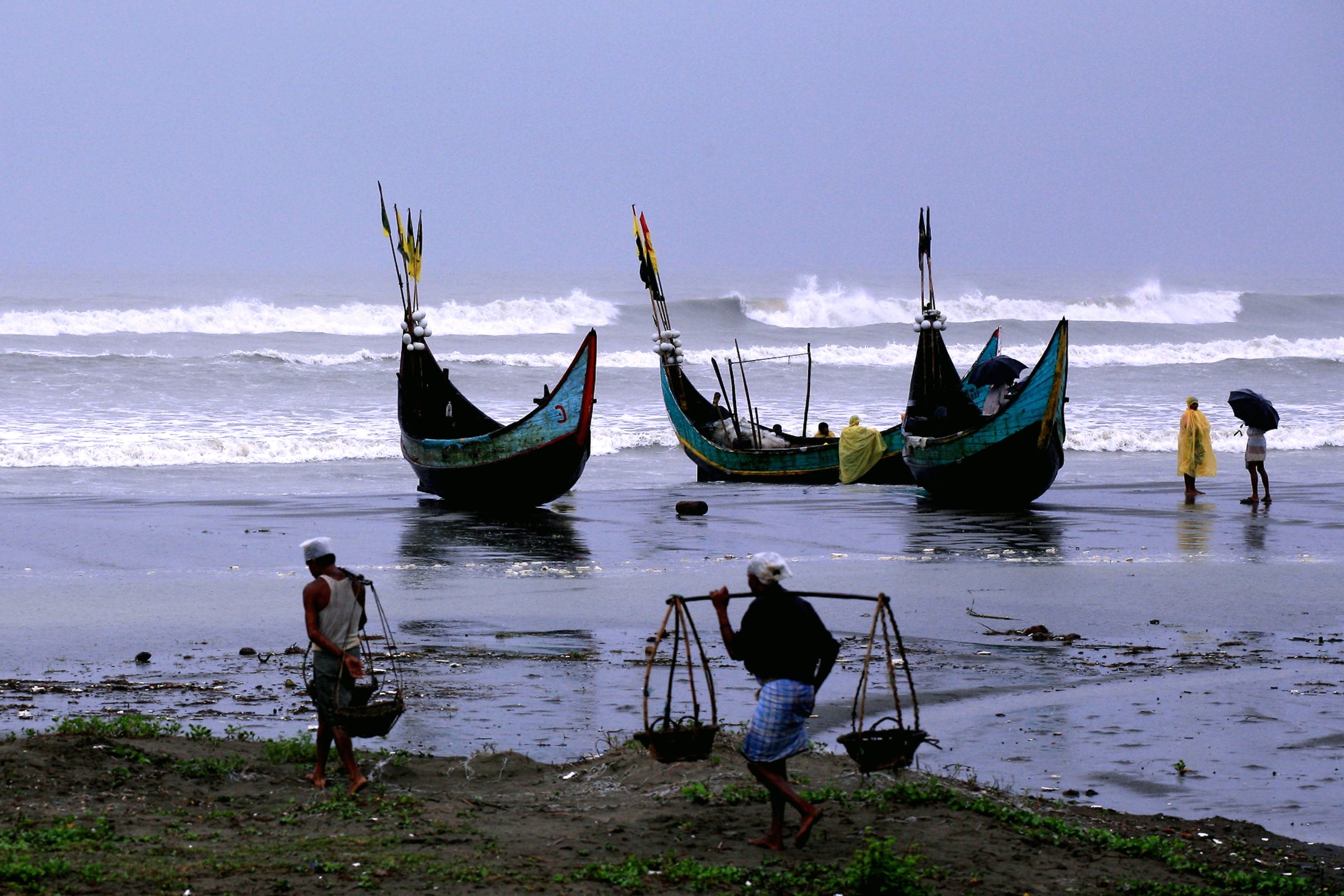 Photograph of traditional fishing boats and people carrying fish on the beach in Bangladesh.