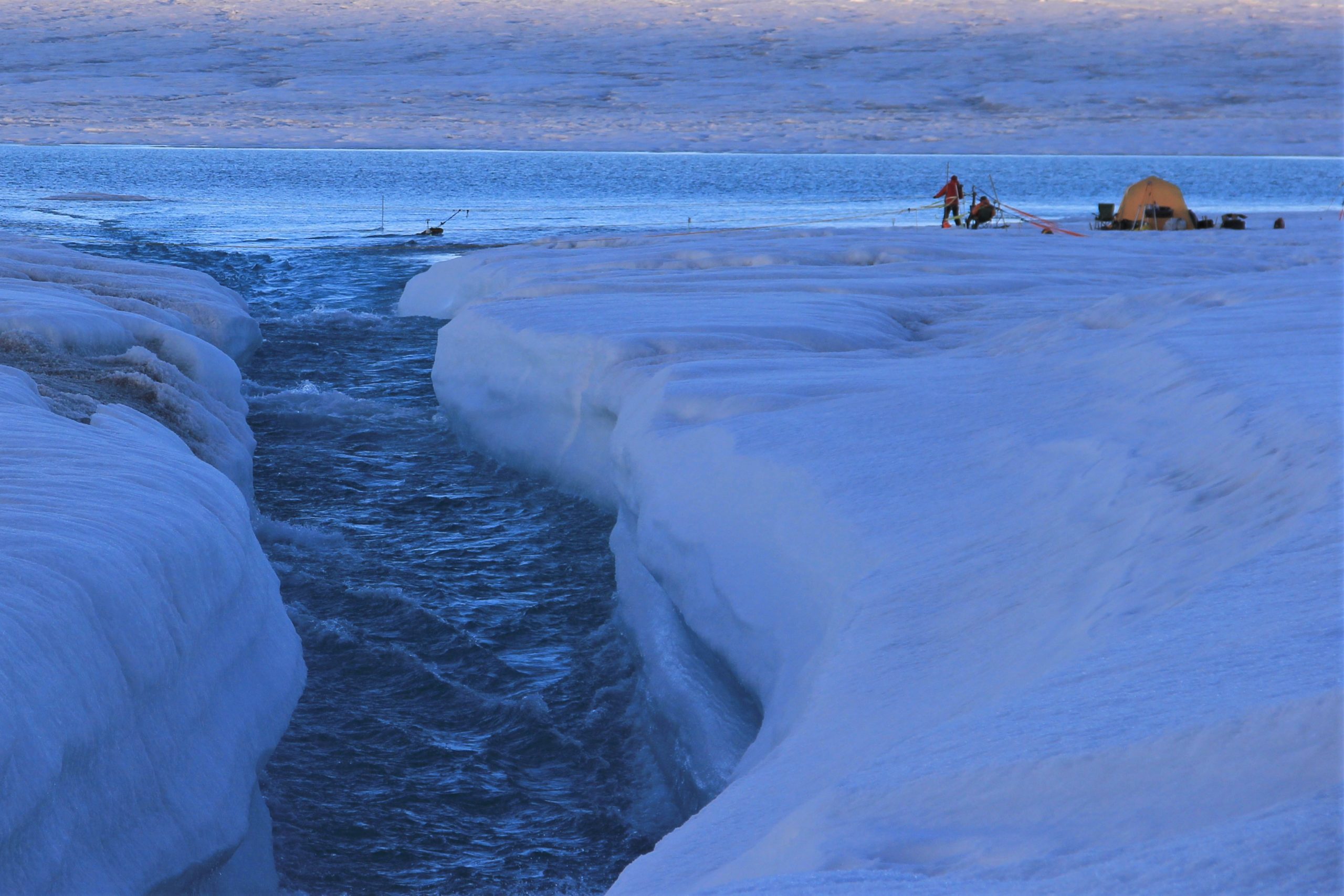 image of a river rushing out of a lake on meltwater on Russell Glacier, Greenland, with silhouettes of researchers.