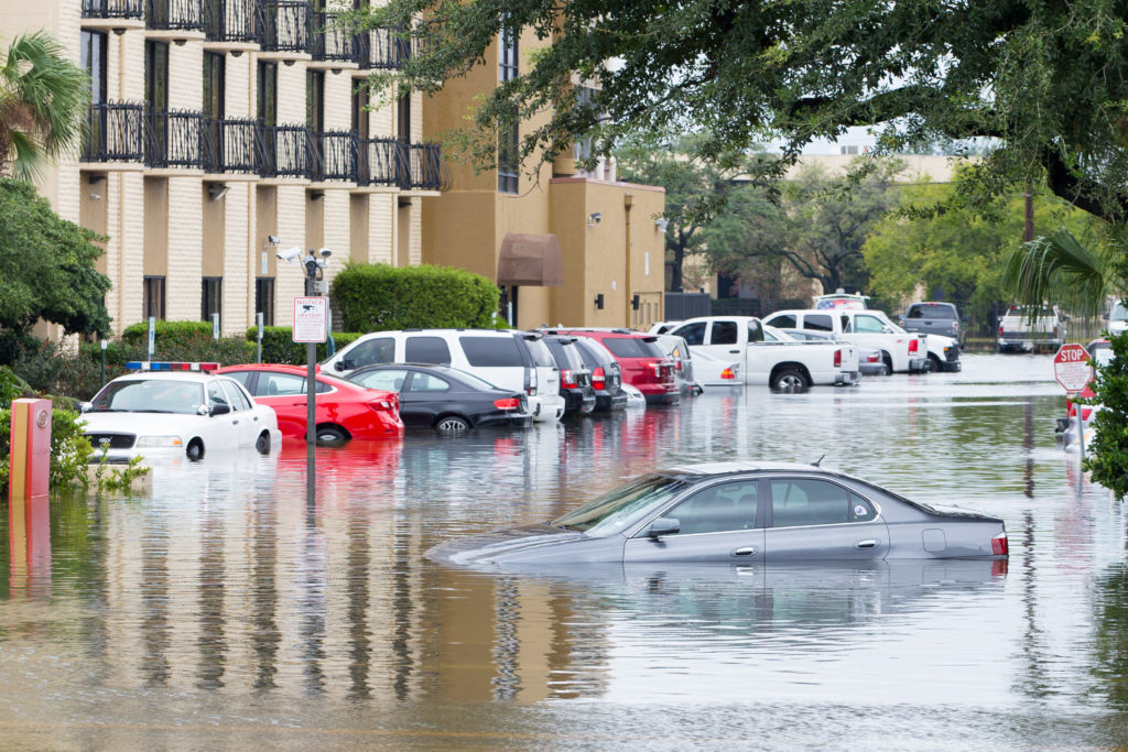 Cars are submerged in a flooded parking lot, next to an apartment building.
