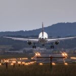 An airplane lands on a runway at dusk. Small hills are in the background.