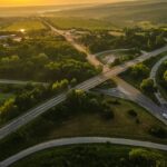 An aerial view of crisscrossing highways. The sun is setting and there are green fields and trees in the background.