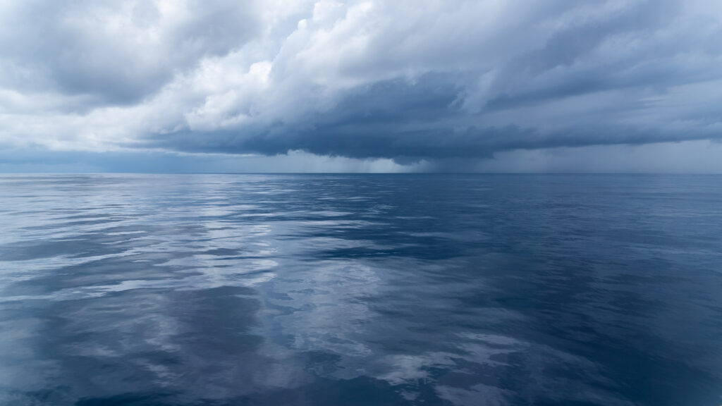 A view of a calm ocean, with storm clouds in the background.