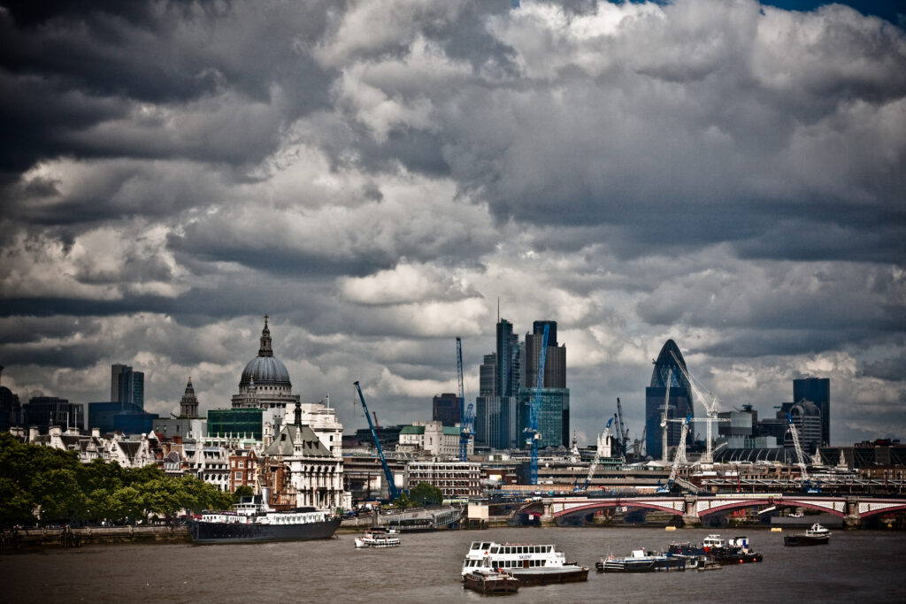 A view of London from the Thames River. Large storm clouds hang over the city.