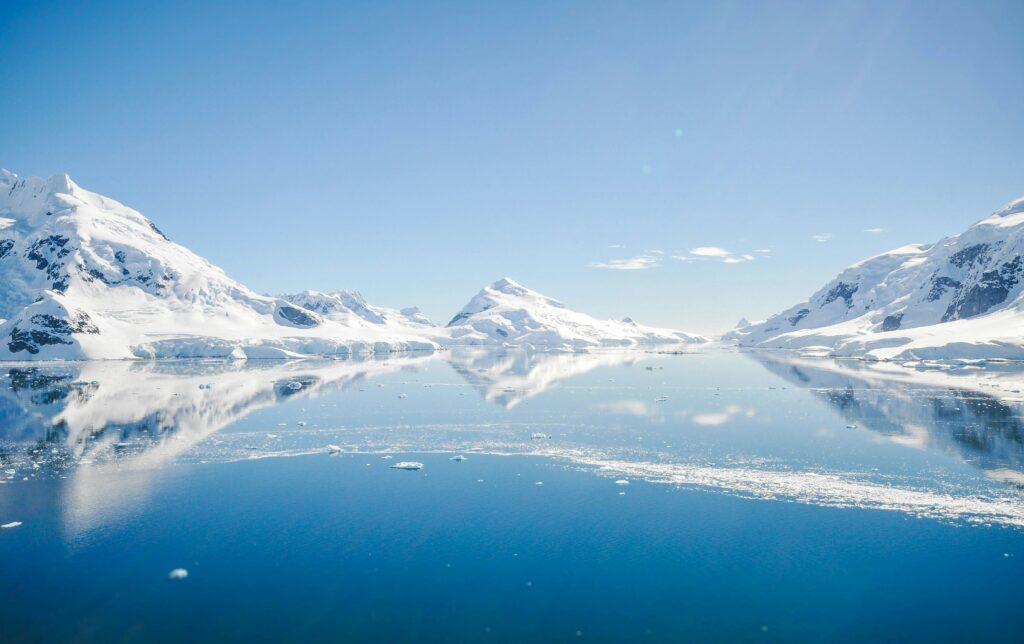 Snow-covered rocky land surrounds a blue bay of water in Antarctica.