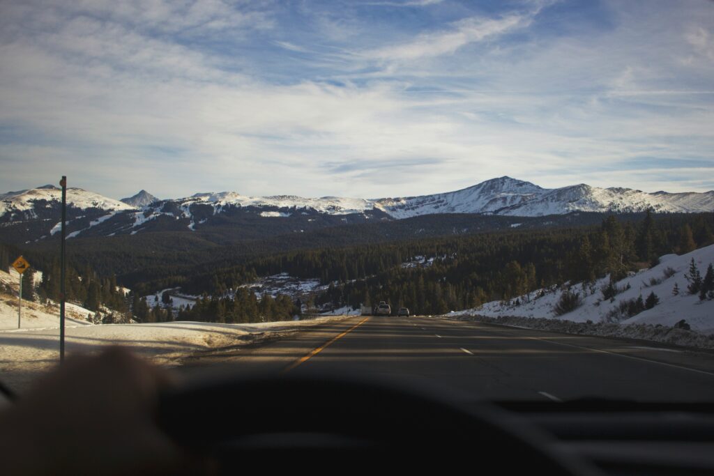 A car drives on a road toward a snowy mountain range.