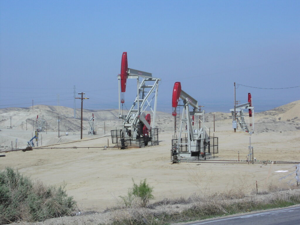 Three oil pumps in a dry landscape, under a blue sky.