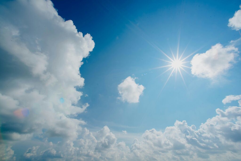 The Sun shining in a blue sky dotted with clouds.