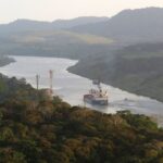 A photograph of a cargo barge floating down the Chagres River in Panama. It is a misty day and green, forest covered hills rise on either side of the river.