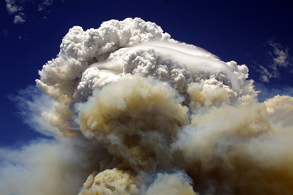 Photo: plumes of white clouds and brownish smoke against a blue sky.