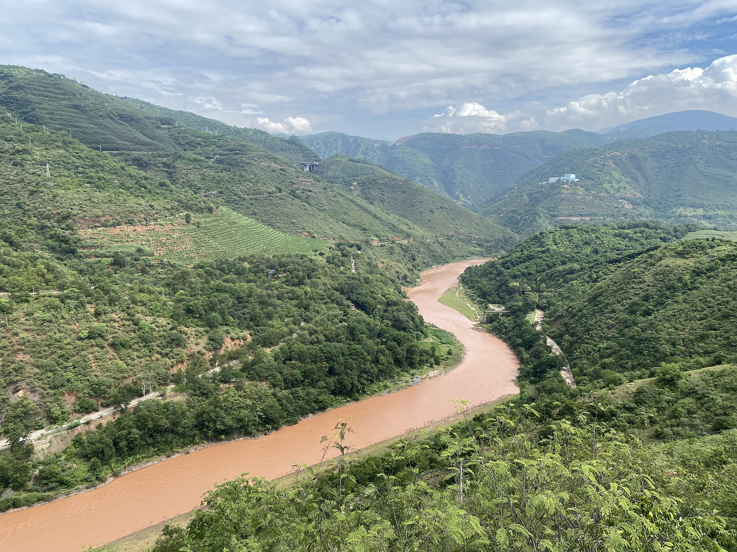photograph: a red-brown river snakes through terraced green hills.