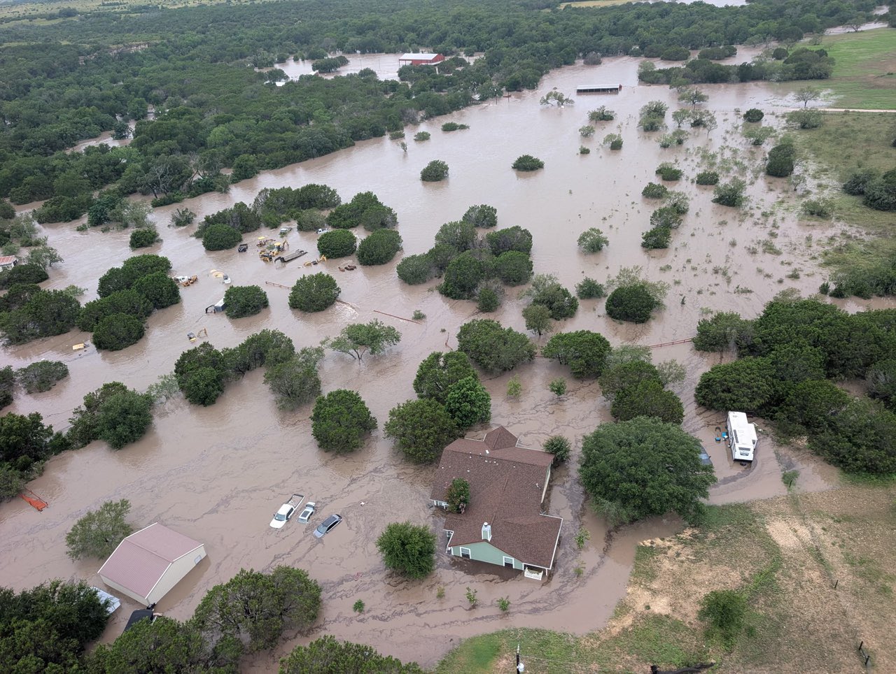 an aerial view of the flooding of the Guadalupe River near Kerrville, Texas, showing inundated homes, vehicles, fields and trees