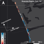 A map that shows the Roanoke dam in a straight line. The map is in black and gray, but along the map where the dam is in a line there are little colored dots. Along the north end of the dam the dots are light red, orange, and white. Along the southern half, the dots are dark blue and light blue with a few deep red clustered together.