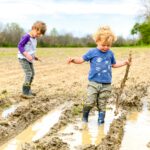 Two young children playing in a muddy field on a sunny day