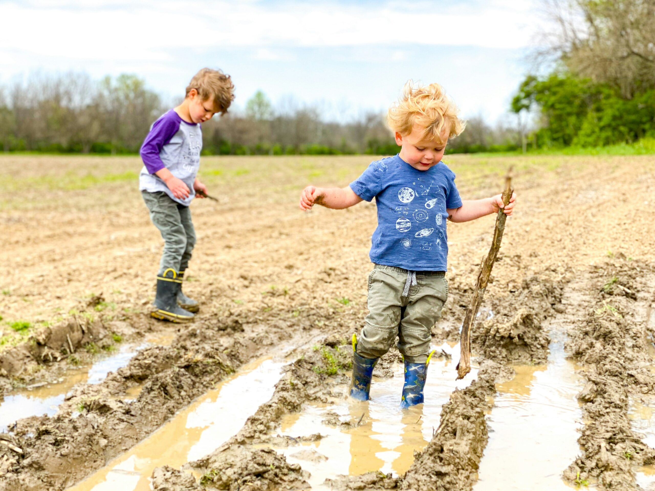 Two young children playing in a muddy field on a sunny day
