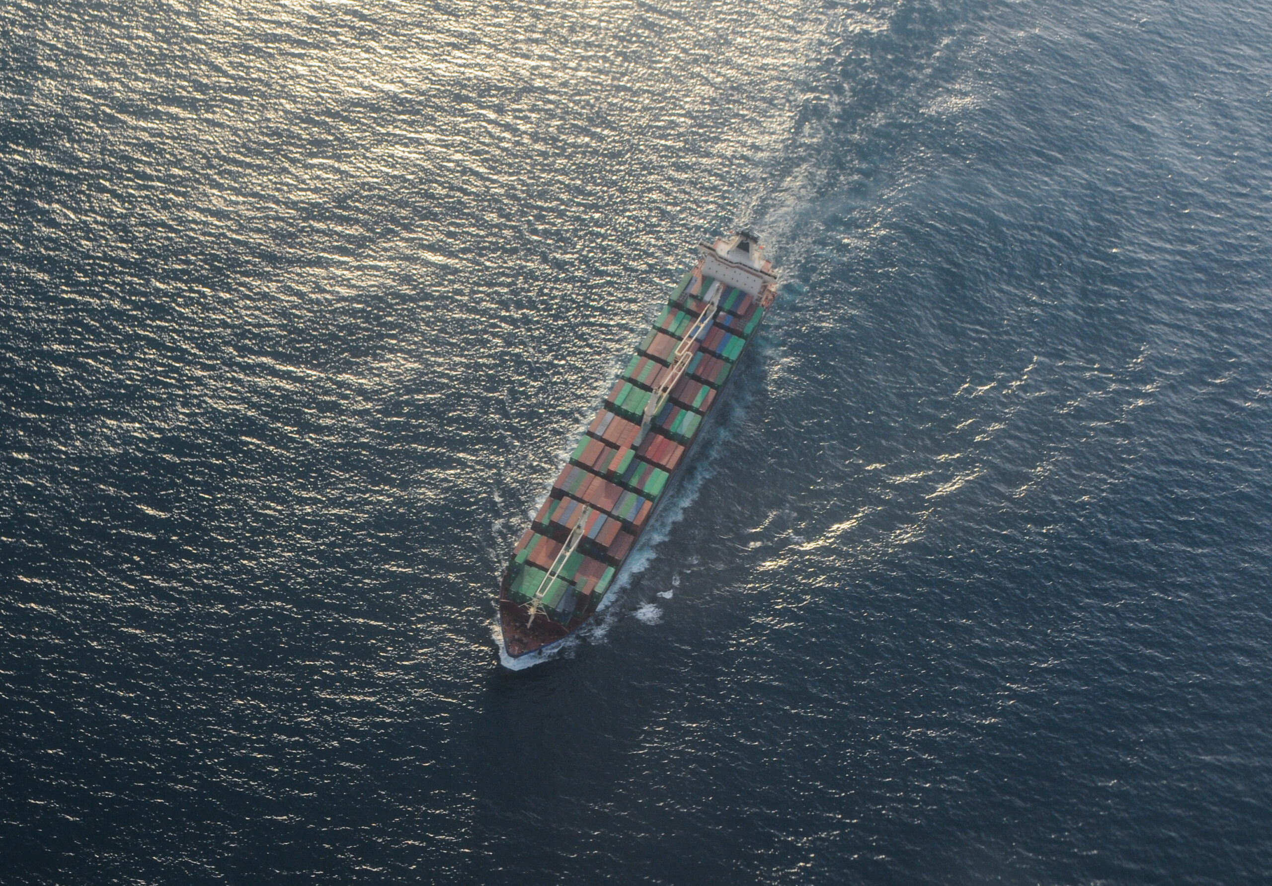A cargo ship in the ocean, loaded with containers, seen from a bird's-eye view in the evening