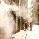 A hot, sunny street in Italy with pedestrians walking under cooling water mist.