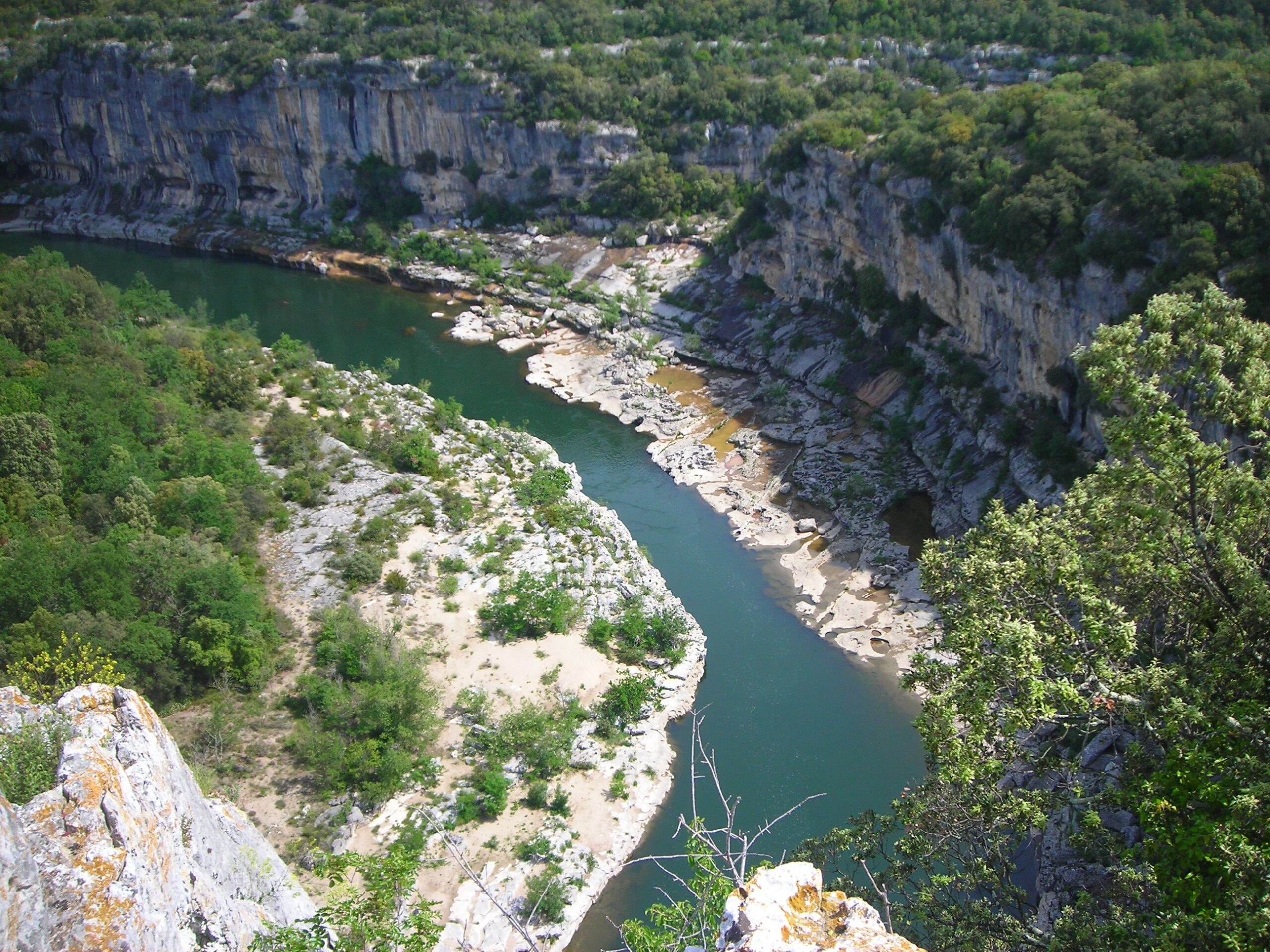 A teal stretch of river at the base of white cliffs topped with trees and plants in the south of France.